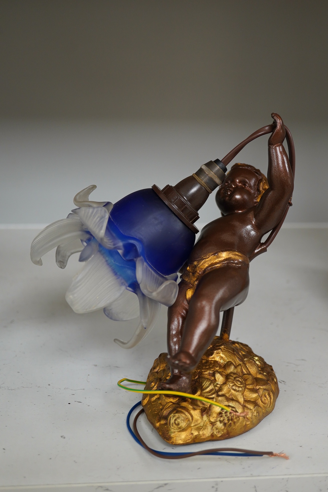 A French bronzed gilded wall light cherub with blue and frosted glass petal shade, circa 1920’s, wired, projection, 24cm. Condition - good